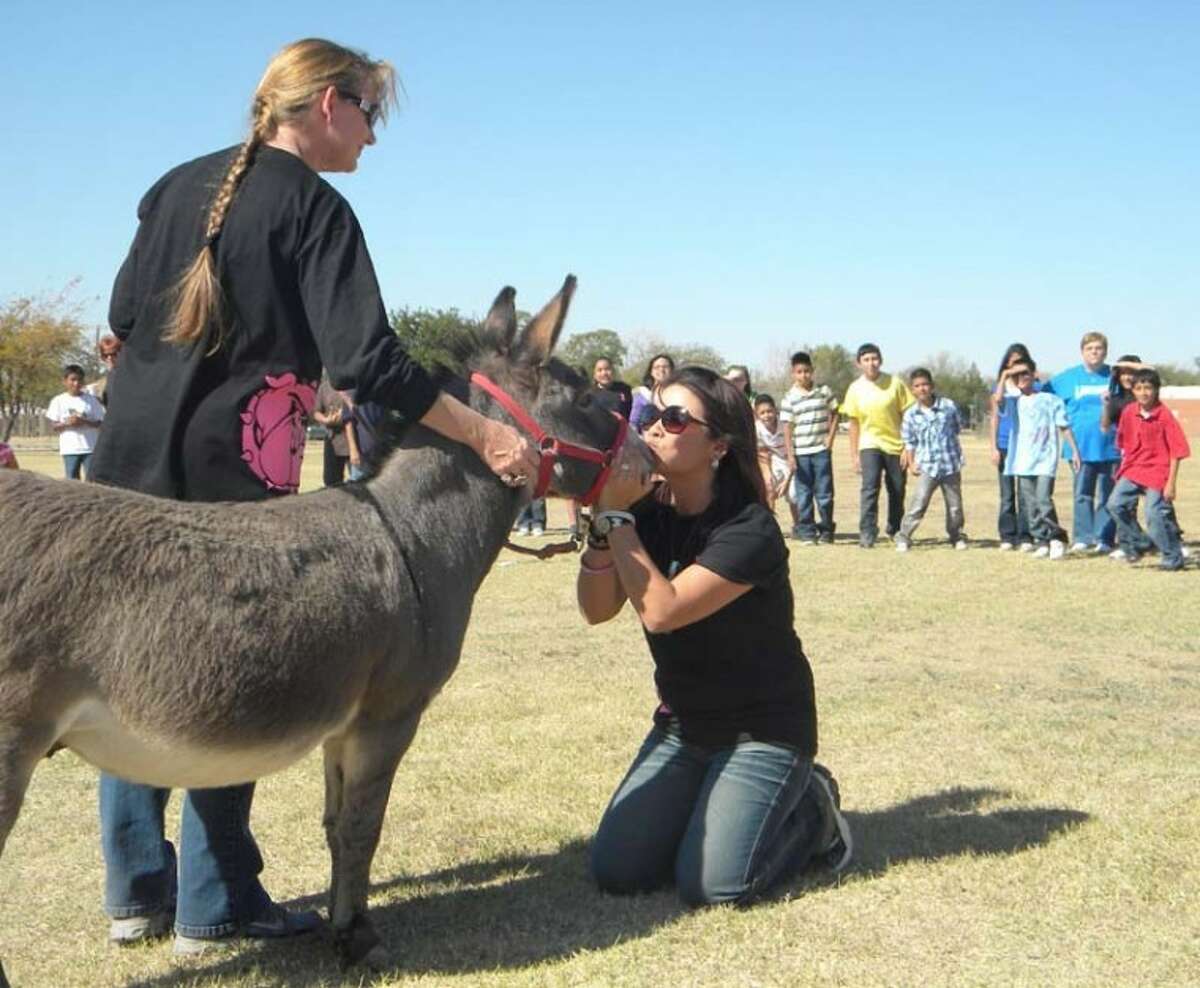 Students at Lakeside Fifth Grade Learning Center watch as school secretary Lisa Wright (left) holds Tex the donkey while Principal Sylvia Suarez gives him a kiss. Students collected more than $500 for United Way during their annual Kiss Tex fundraiser, bringing their United Way total to $1,200.