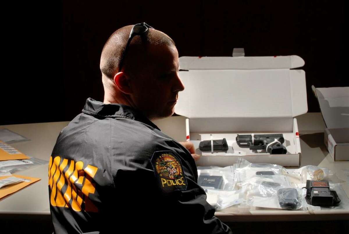 Sgt. Timothy Hilderbrand of the Greenwich Police Department narcotics unit posed at Greenwich Police headquarters Wednesday, April 28, 2010, with evidence seized during drug arrests. In the center of the photo is a Glock handgun. Hilderbrand asked that his face be hidden from view.