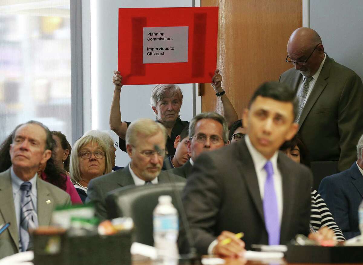 During a briefing on the San Antonio Comprehensive Plan before the City Council, Alamo Group of the Sierra Club member Meredith McGuire protests with a sign reading: “Planning Commission Impervious to Citizens.” A reader argues that economic output should be about people, not just development.