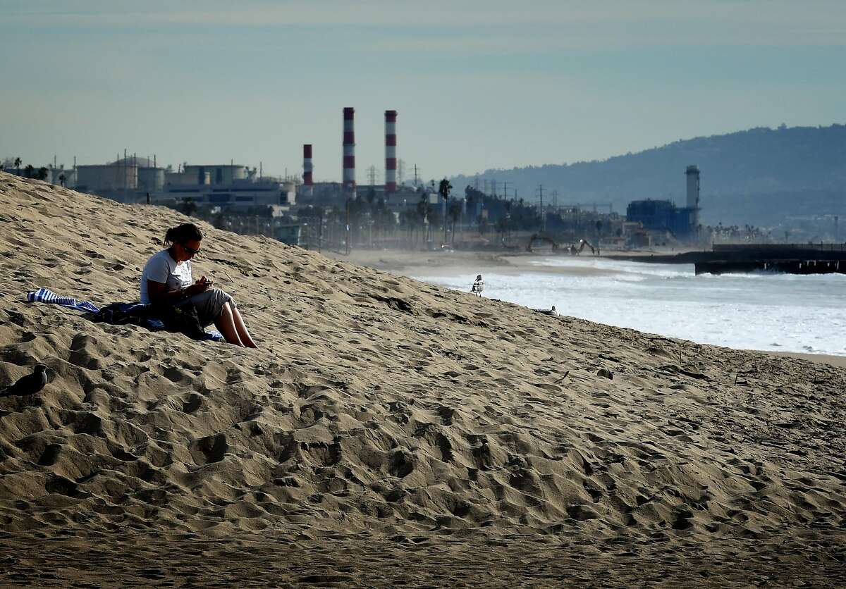A woman sits on a sand berm created by city workers to protect houses from El Nino storms and high tides at Playa Del Rey beach in Los Angeles, California on November 30, 2015, at the start of the COP21 conference in Paris. Some 150 leaders, including US