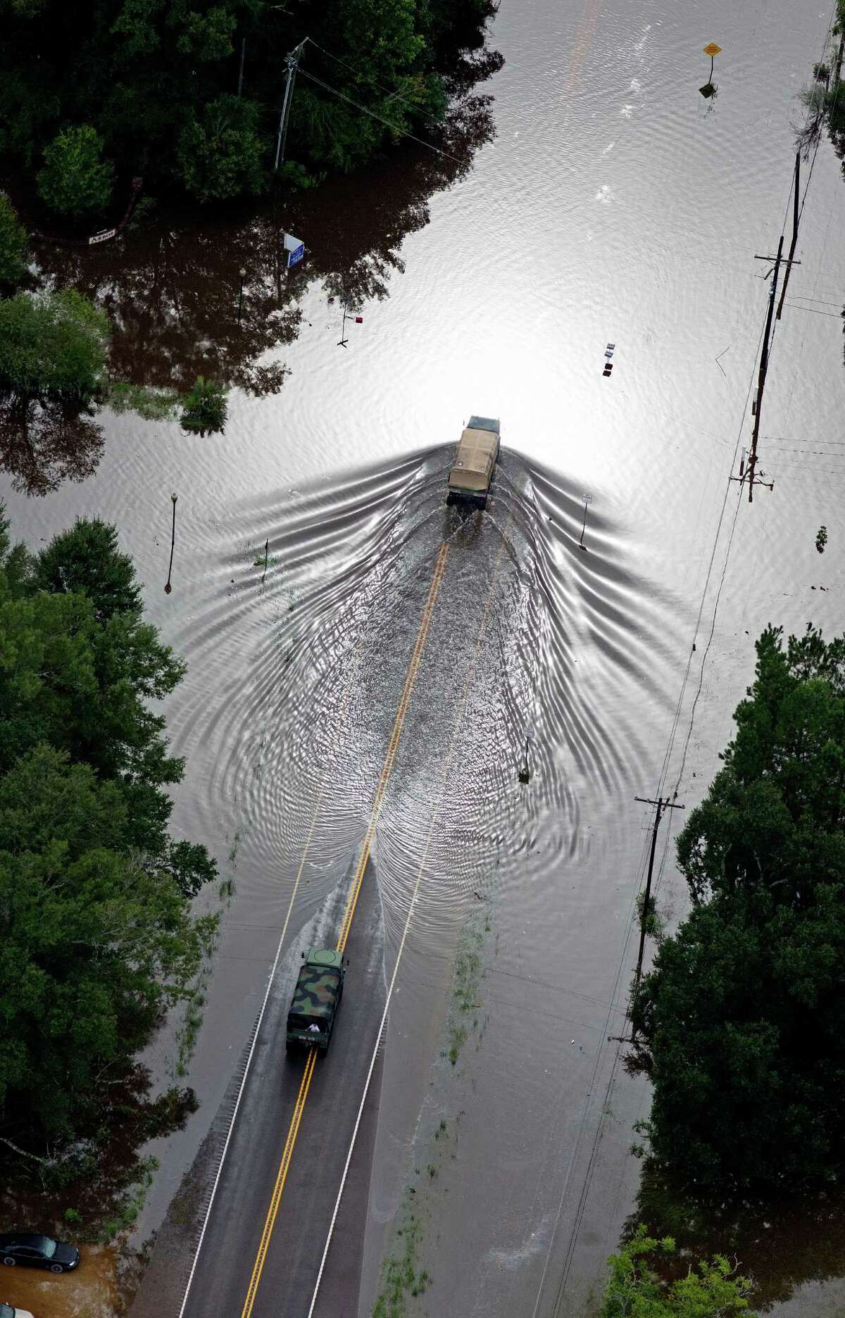 In this aerial photo over Robert, La., Army National Guard, vehicles drive on flooded U.S. Route 190 after heavy rains inundated the region, Saturday, Aug. 13, 2016. Louisiana Gov. John Bel Edwards says more than 1,000 people in south Louisiana have been rescued from homes, vehicles and even clinging to trees as a slow-moving storm hammers the state with flooding. (AP Photo/Max Becherer)