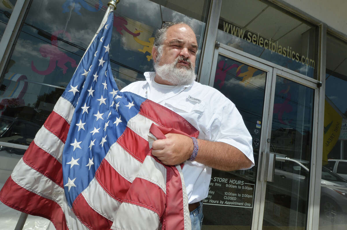 Tony D'Andrea holds the American flag in front of his business, Select Platics LLC in Liberty Square in Norwalk. Tony has been displaying flags and signs because the State of Connecticut was going to take his property to provide access to rebuild the Walk Bridge over the Norwalk River near his shop. The state has decided to not take his property but will need properties in the area of Goldstein Place on Monday August 15, 2016 in Norwalk Conn.