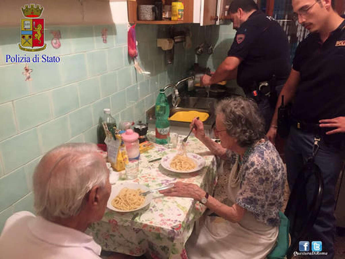 In this recent photo made available by the Italian Police, two police officers serve pasta, after cooking it, to two elderly, after they were called in a Rome neighborhood to check on a couple loudly quarreling on a recent, hot summer night. Police say that four officers who came to the couple's apartment used butter, cheese, spaghetti and "all their humanity" to cook them dinner and ease their loneliness. (Italian Police Photo via AP)