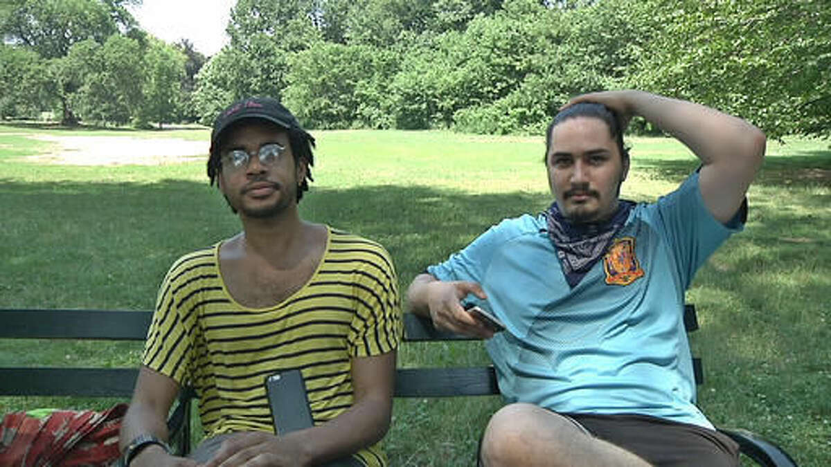 In this July 13, 2016 frame grab from video, Jordan Clark, left, and Lewis Gutierrez sit in Prospect Park as they talk about their new "Pokemon Go" business in the Brooklyn borough of New York. They are among the new entrepreneurs who offer their services as "trainers" for the game at $20 per hour - logging onto a client's "Pokemon Go" account and effectively running up their score while a client is stuck at work or sitting in class. (AP Photo/Ezra Kaplan)