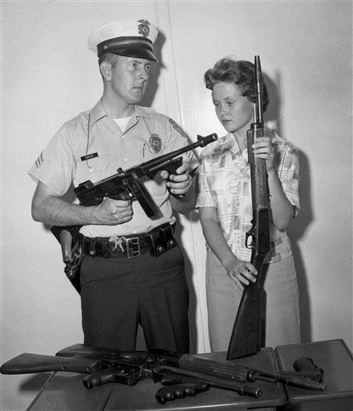 In this 1961 photo, Tucson Police Sgt. Tom Keeley holds a Colt Thompson submachine gun and secretary Linda Bradfield holds a Winchester Model 1907, with other guns confiscated from the John Dillinger gang during Dillinger's capture in Tucson, Ariz., in 1934. Police in Tucson are at odds with a small Indiana town over the Tommy gun taken from Dillinger during his arrest. The Arizona Daily Star reports that officials in Peru, Ind., want the Colt Thompson submachine gun turned over, saying they believe it was stolen from Peru police in 1933 before Dillinger was caught in Tucson. (Tucson Citizen Archive/Arizona Daily Star via AP)