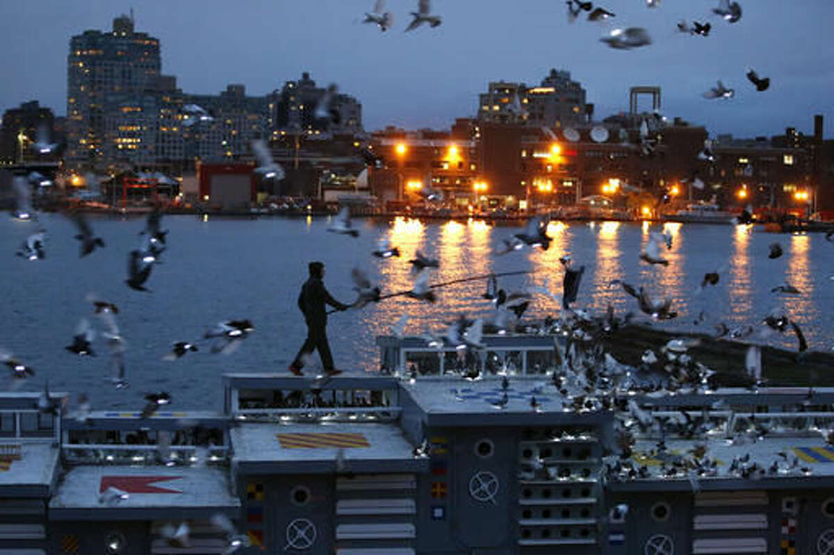 Artist Duke Riley rouses some of the 2,000 pigeons wearing LED lights to fly above their coops on board the Baylander, a decommissioned naval ship docked at the Brooklyn Navy Yard, Thursday, May 5, 2016, in New York. The 30-minute performance was part of Riley's "Fly By Night," creation. (AP Photo/Kathy Willens)