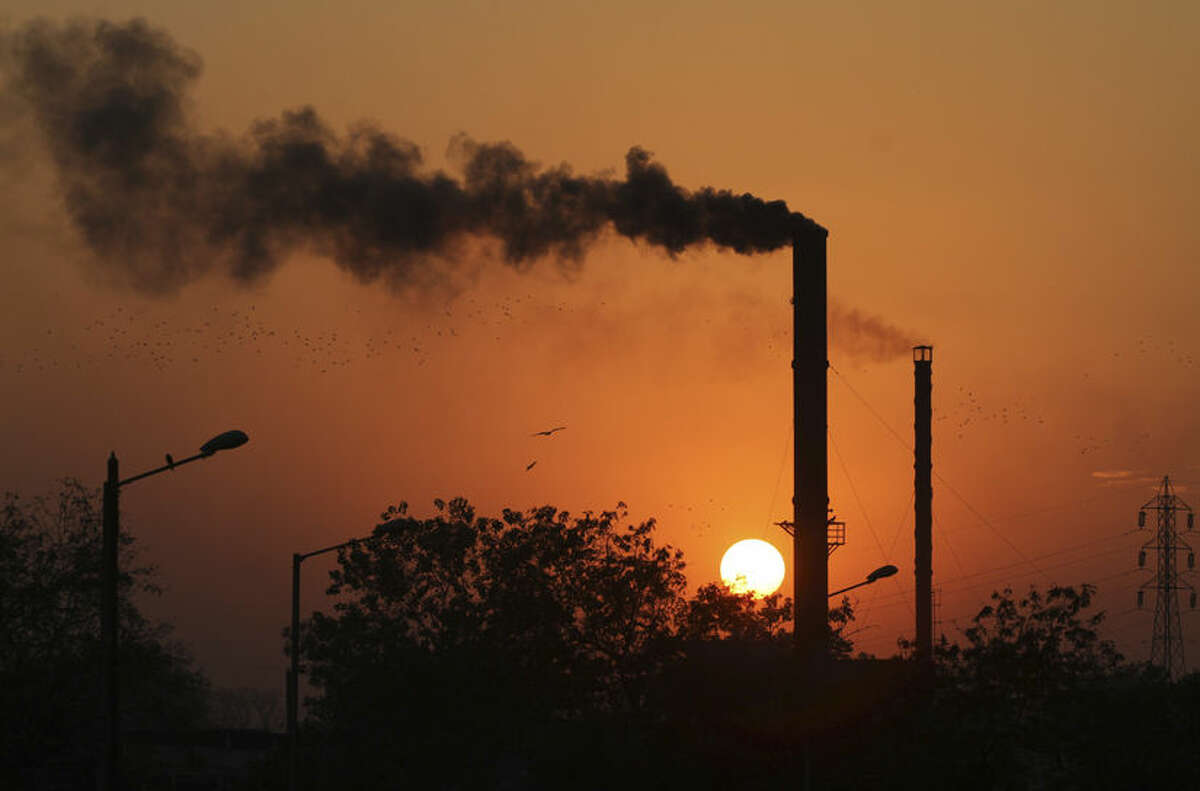 FILE - This is a Monday, Dec. 8, 2014 file photo of birds as they fly past at sun set as smoke emits from a chimney at a factory in Ahmadabad, India. The U.N.'s scientific panel on climate change will write a special report on how to limit global warming to 1.5 degrees Celsius (2.7 degrees Fahrenheit) compared with pre-industrial times. Temperatures have already risen almost 1 degree C (1.8 F) since humans started burning fossil fuels — the biggest source of greenhouse gases — on an industrial scale in the 19th century. (AP Photo/Ajit Solanki, File)