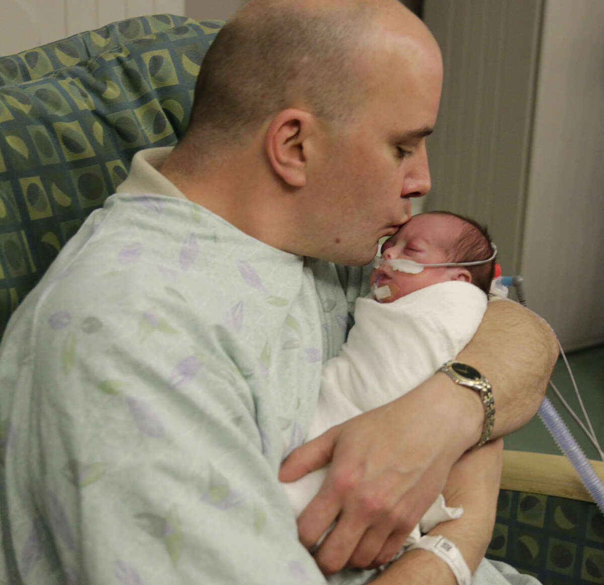 In this Tuesday, March 15, 2016 photo, parent Bryan Niedermeyer holds Evelyn, one of his twin preemie daughters after they underwent eye exams at Advocate Children's Hospital in Chicago. Olivia and Evelyn Niedermeyer are part of recent research showing benefits from low-tech pain management alternatives during necessary procedures on these fragile babies that are poked and prodded as part of medical care meant to help them survive, but can be painful. (AP Photo/M. Spencer Green)