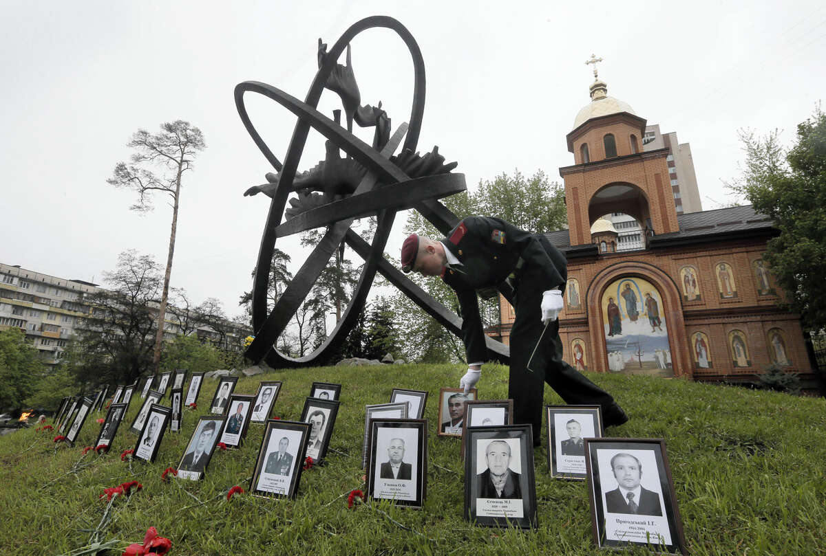 A soldier places portrait photos near the monument erected in memory of the victims of the Chernobyl explosion in Ukraine's capital Kiev, Ukraine, Tuesday, April 26, 2016. Ukraine marks the 30th anniversary of the Chernobyl nuclear disaster, which spread radiation over much of northern Europe. (AP Photo/Efrem Lukatsky)