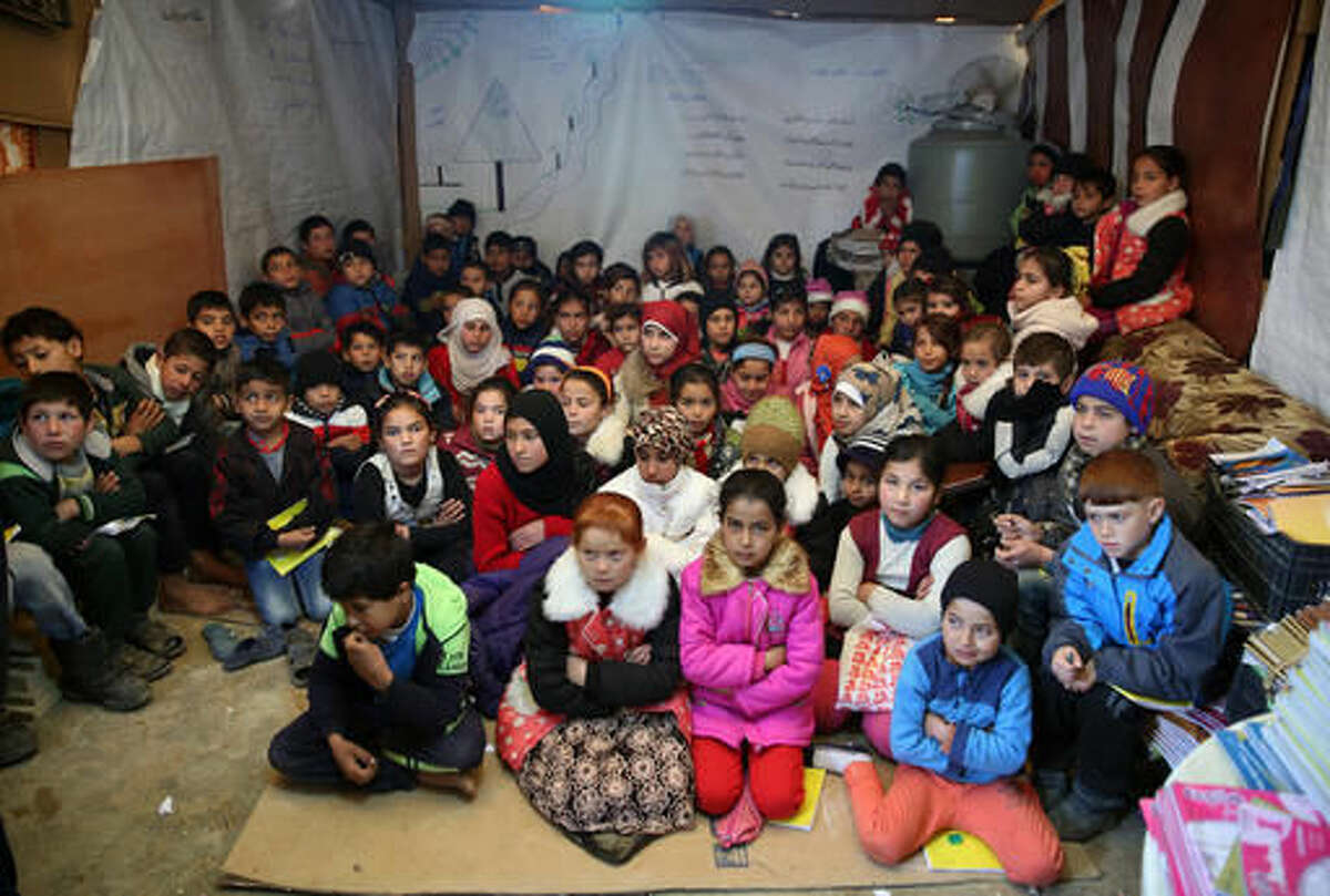 FILE - In this Wednesday, Jan. 27, 2016 file photo, Syrian refugee children sit on the ground as they listen to their teacher inside a tent, home for a refugee family that has been turned into a makeshift school, in a Syrian refugee camp in the eastern town of Kab Elias, Lebanon. School budgets in the Middle East are facing major shortfalls in the run up to the new academic year, leaving some one million Syrian refugee children out of schools, according to a new report by the international children's charity Their World. (AP Photo/Bilal Hussein, File)