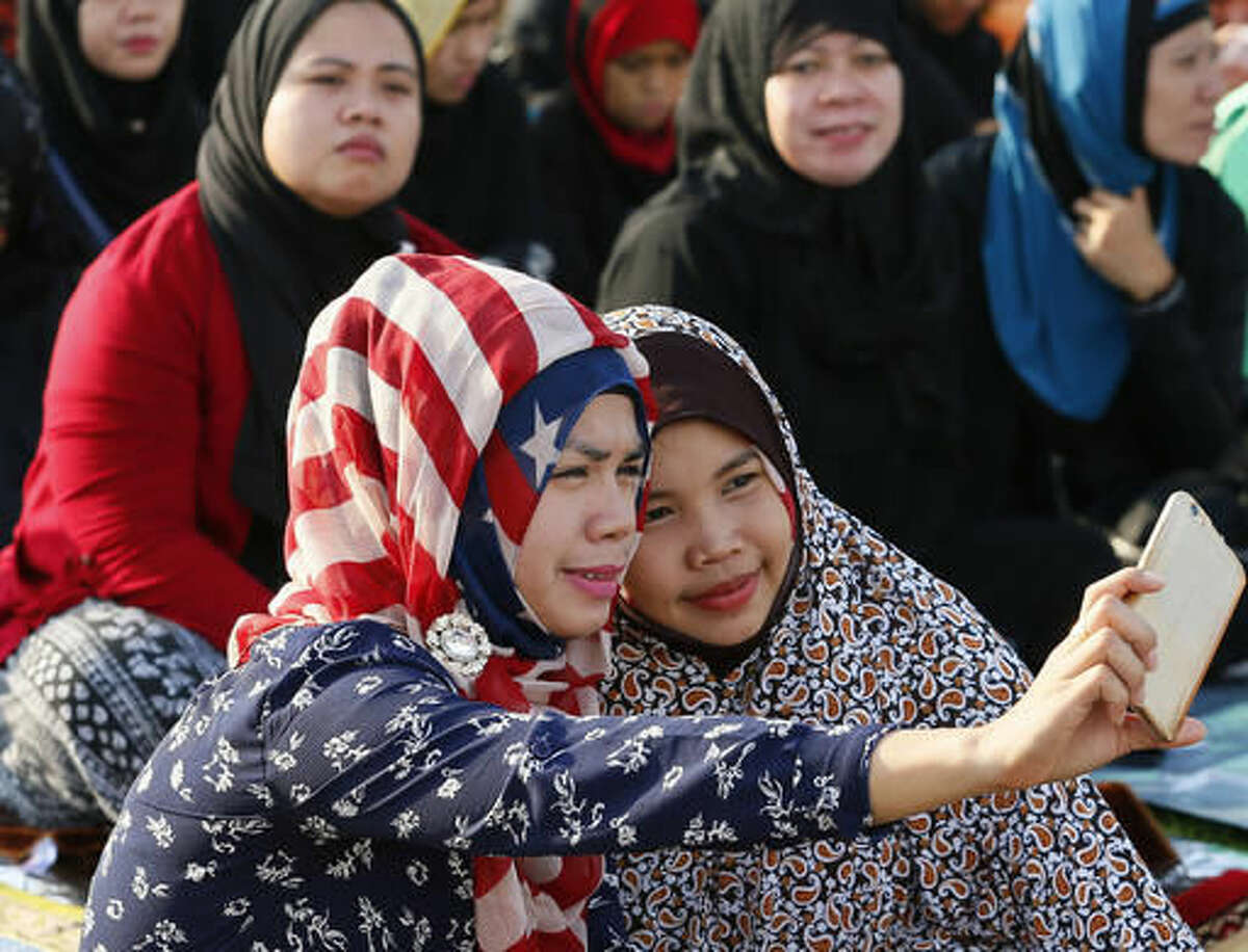 Filipino Muslims take a selfie photo as they gather at Rizal Park for Eid'l Fitr, to mark the end of the holy month of Ramadan in Manila, Philippines, on Wednesday, July 6, 2016. The rest of the world may think Americans eat a lot of burgers, have huge shopping malls and are ruled by an arrogant government. And yet the “Ugly American,” it would seem, isn't all bad. Americans are also seen from afar as generous tippers, friendly, uncomplicated, rich and the standard bearers of freedom, equality, creativity and technological power. (AP Photo/Bullit Marquez)