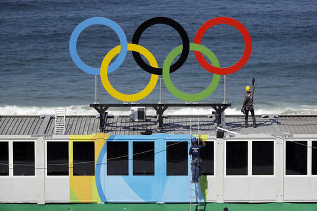 Workers install Olympic rings with the ocean as a backdrop during a training session at Copacabana beach volleyball arena at the 2016 Summer Olympics in Rio de Janeiro, Brazil, Friday, Aug. 5, 2016. (AP Photo/Marcio Jose Sanchez)