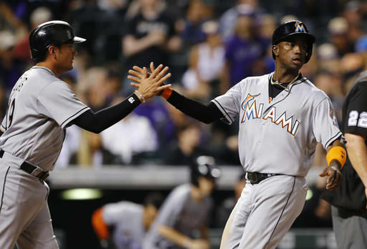 Miami Marlins' Miguel Rojas, left, and Adeiny Hechavarria celebrate scoring on a Martin Prado two RBI single against Colorado Rockies relief pitcher Carlos Estevez during the ninth inning of a baseball game Friday, Aug. 5, 2016, in Denver. (AP Photo/Jack Dempsey)