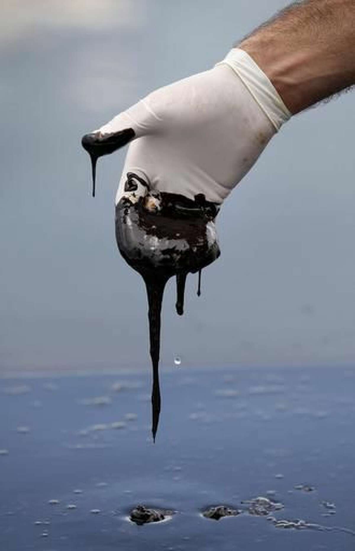 FILE - In this June 15, 2010 file photo, a member of Louisiana Gov. Bobby Jindal's staff reaches into thick oil on the surface of the northern regions of Barataria Bay in Plaquemines Parish, La. Big Oil's legacy in Louisiana _ an industry long blamed for causing land loss in the coast, is now in dispute like never before. What's changed is the person in the governor's mansion: After eight years of Republican rule, a Democrat is in the mansion. (AP Photo/Gerald Herbert, File)