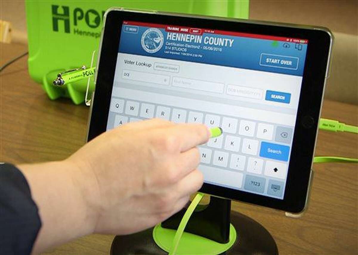 Election Manager for Hennepin County Jinny Gelms demonstrates how to use an e-poll book program on Aug. 4, 2016 in Minneapolis. Poll workers will replace the paper rosters with electronic tablets when voters check in or are registered and when they log absentee ballots. The electronic poll book stations will be used around Hennepin County with the exception of Minneapolis, which plans to introduce the e-poll books next year. (Matt Gillmer/Star Tribune via AP)