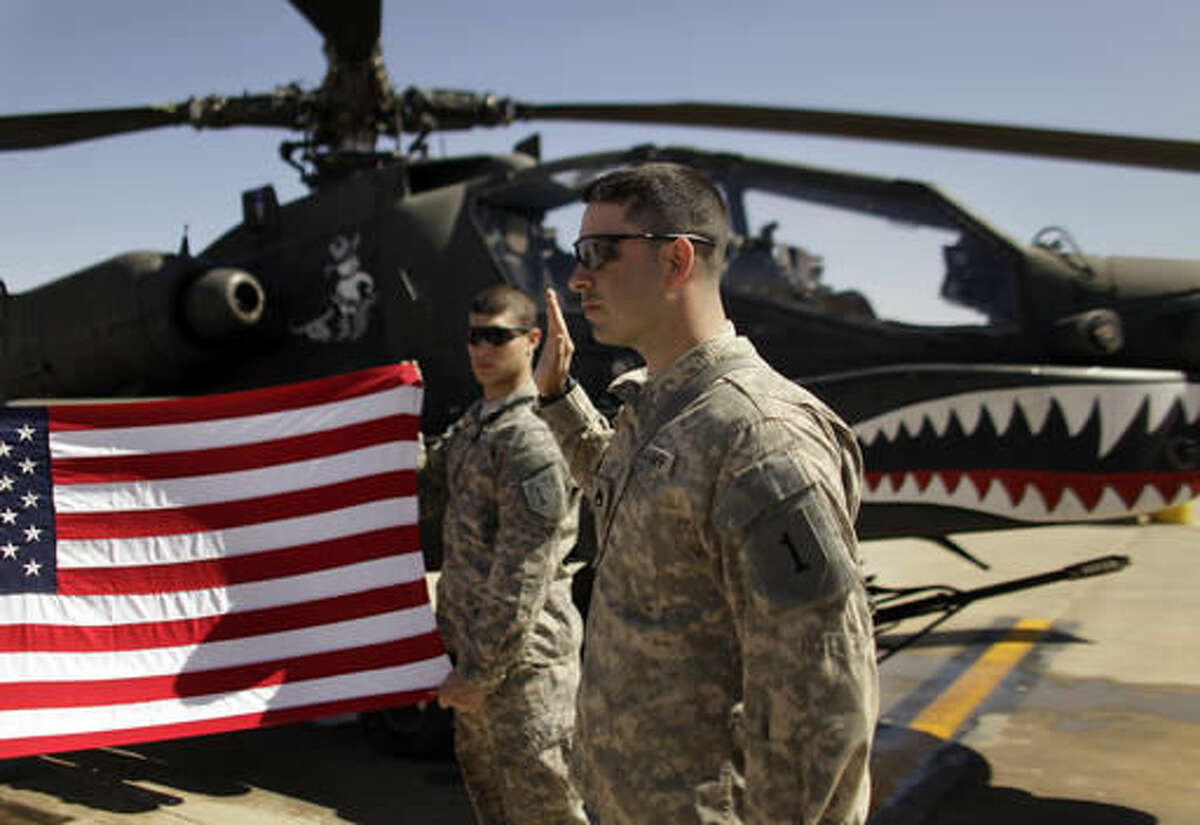In this March 16, 2011, file photo Army Staff Sgt. Christopher Seeman, right, of Kalispell, Mont., takes the oath of re-enlistment as Spc. Brian Martinez, center, of Aurora, Ill., holds up a American flag in front of an Apache helicopter during a ceremony at Camp Taji, north of Baghdad, Iraq. The way America wields its power around the world affects people in every walk of life, in every corner of the country. Going to war in Afghanistan in 2001 and Iraq in 2003 profoundly changed the lives of tens of thousands of people whose loved ones were killed or grievously wounded. It also raised questions that confront Hillary Clinton and Donald Trump: How can American influence be used most effectively to protect the homeland and prevent future wars? (AP Photo/Maya Alleruzzo, File)