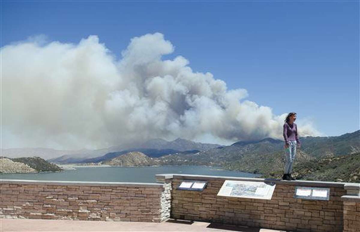 A wildfire burns in the background behind a sightseer as smoke billows over Silverwood Lake on Sunday afternoon, Aug. 7, 2016, in Crestline, Calif. A rapidly growing forest fire in Southern California is burning about 55 miles east of Los Angeles in a remote area near Silverwood Lake, a state recreation area, near the small mountain community of Crestline. A massive plume of smoke could be seen blowing north toward the Mojave Desert. (James Quigg/The Daily Press via AP)