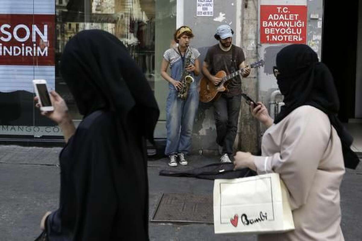 Tourists check their cellphones as street artists play music in Istanbul, Tuesday, Aug. 9, 2016. Life has returned to normal, although a welling up of national pride and broad support for actions against the perpetrators of the failed July 15 military coup attempt, has drawn daily street demonstrations in support of the government. (AP Photo/Thanassis Stavrakis)