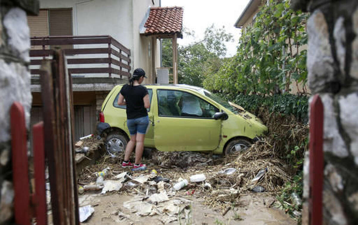 A woman stands by a damaged car in the house yard after flooding, in the village of Stajkovci, just east of Skopje, Macedonia, on Monday, Aug. 8, 2016. Macedonia's government declared a state of emergency Sunday in parts of the capital hit by torrential rain and floods that left at least 21 people dead, six missing and dozens injured, authorities said. (AP Photo/Boris Grdanoski)