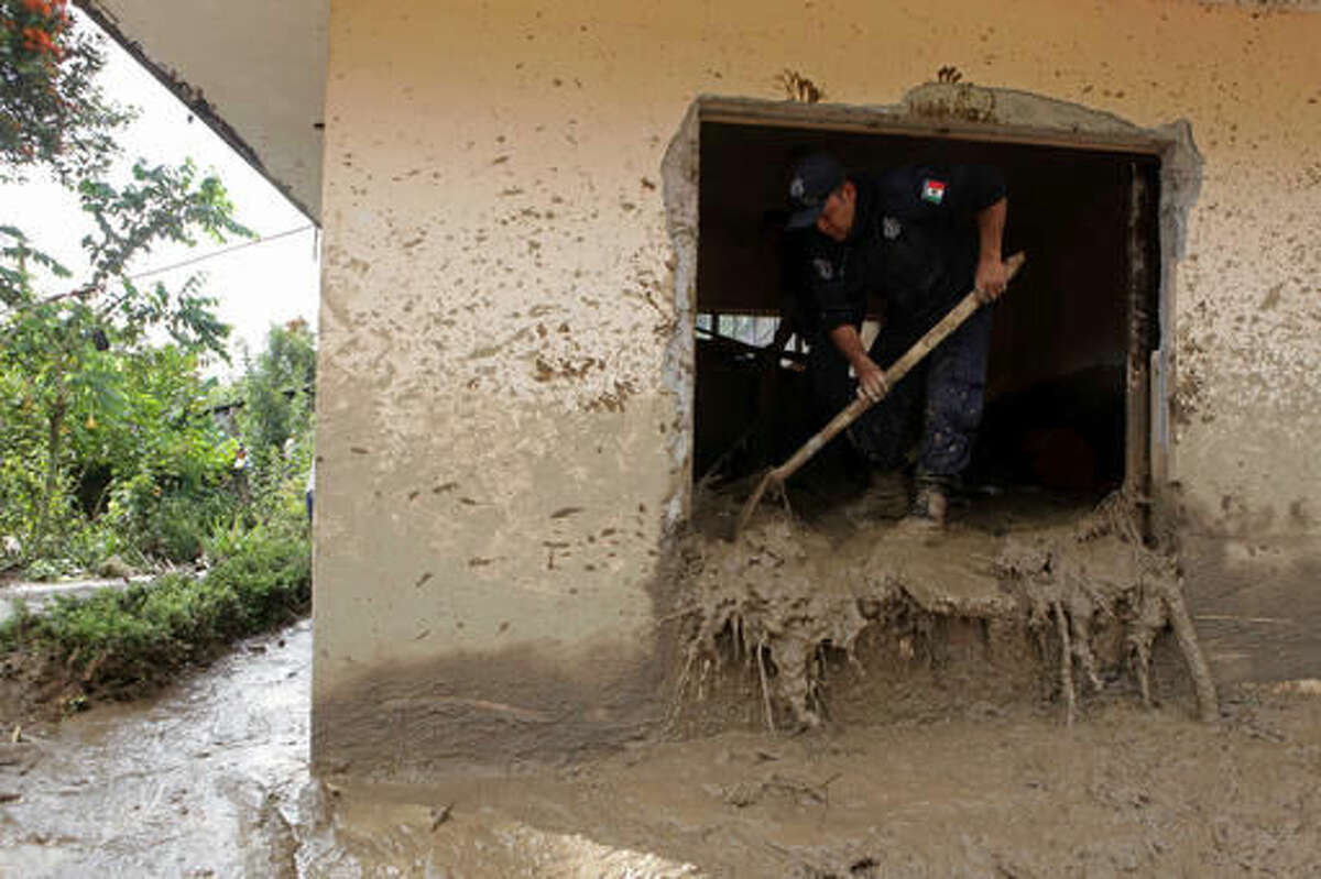 A federal agent removes mud from a house damaged by a mudslide in Xaltepec, Mexico, Monday, Aug. 8, 2016. Mountain communities in two Mexican states are recovering from weekend mudslides that killed dozens during heavy rains brought by remnants of Hurricane Earl. (AP Photo/Pablo Spencer)