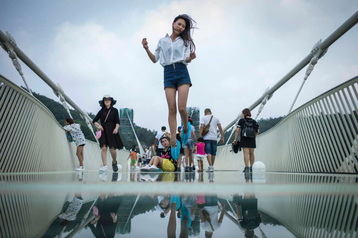 A visitor jumps for a photograph on the world's highest and longest glass-bottomed bridge above a valley in Zhangjiajie in China's Hunan Province on August 21, 2016.