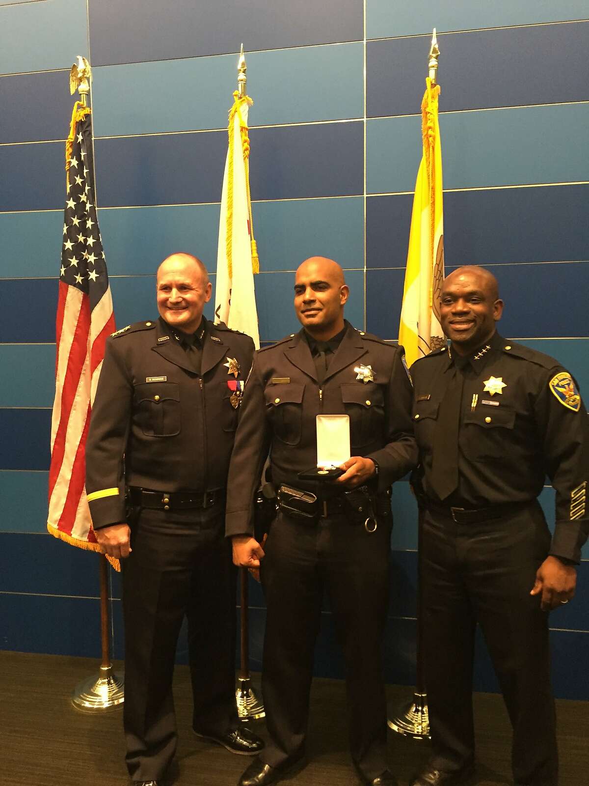 Off. Riley Bandy of the San Francisco Police Department (center) after receiving an award on Sept. 2 at SFPD headquarters for foiling an armed robbery while off-duty in Oakland during the summer. With him are Assistant Chief David Downing of the Oakland Police Department (left) and the SFPD's acting chief, Toney Chaplin