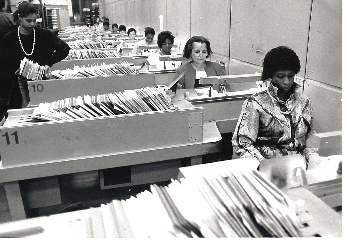 A photo of a crowded Atlantic Street post office on Dec. 21, 1987. In the foreground to the right, Kim Lee works with others sorting mail through machines.