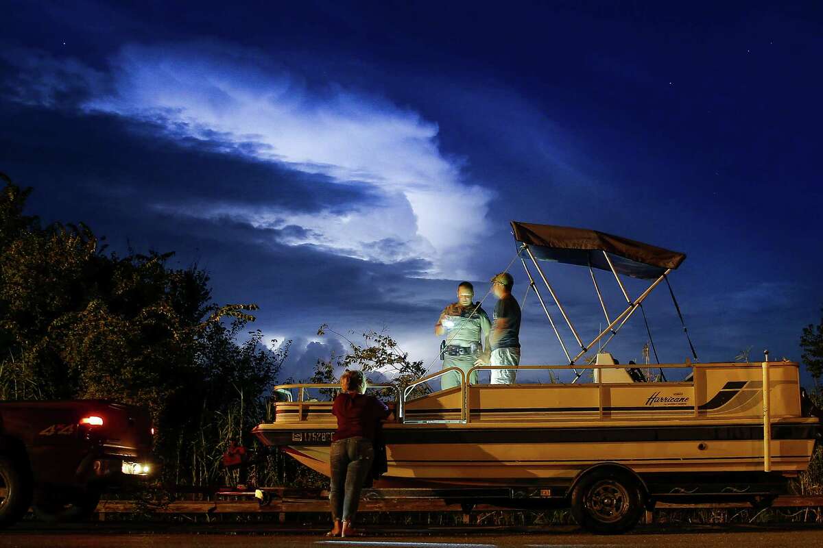 Lightning fills the sky as Texas Game Warden Dustin Dockery, center, talks to a man and woman who were pulling their boat out of the Trinity River at the Wallisville Lake Project Friday, August 26, 2016. The man and woman admitted to fishing without licenses and littering and Dockery also discovered that the boat registration was expired and the truck they were driving did not have insurance.