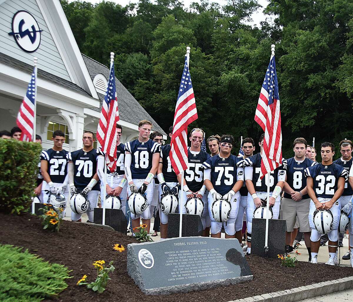 The Wilton High football team stands silently as a memorial stone for former head coach Tom Fujitani is revealed before the start of Friday's season-opening game against Fairfield Warde, which was played on Fujitani Field. Theformer coach passed away suddenly earlier this year.