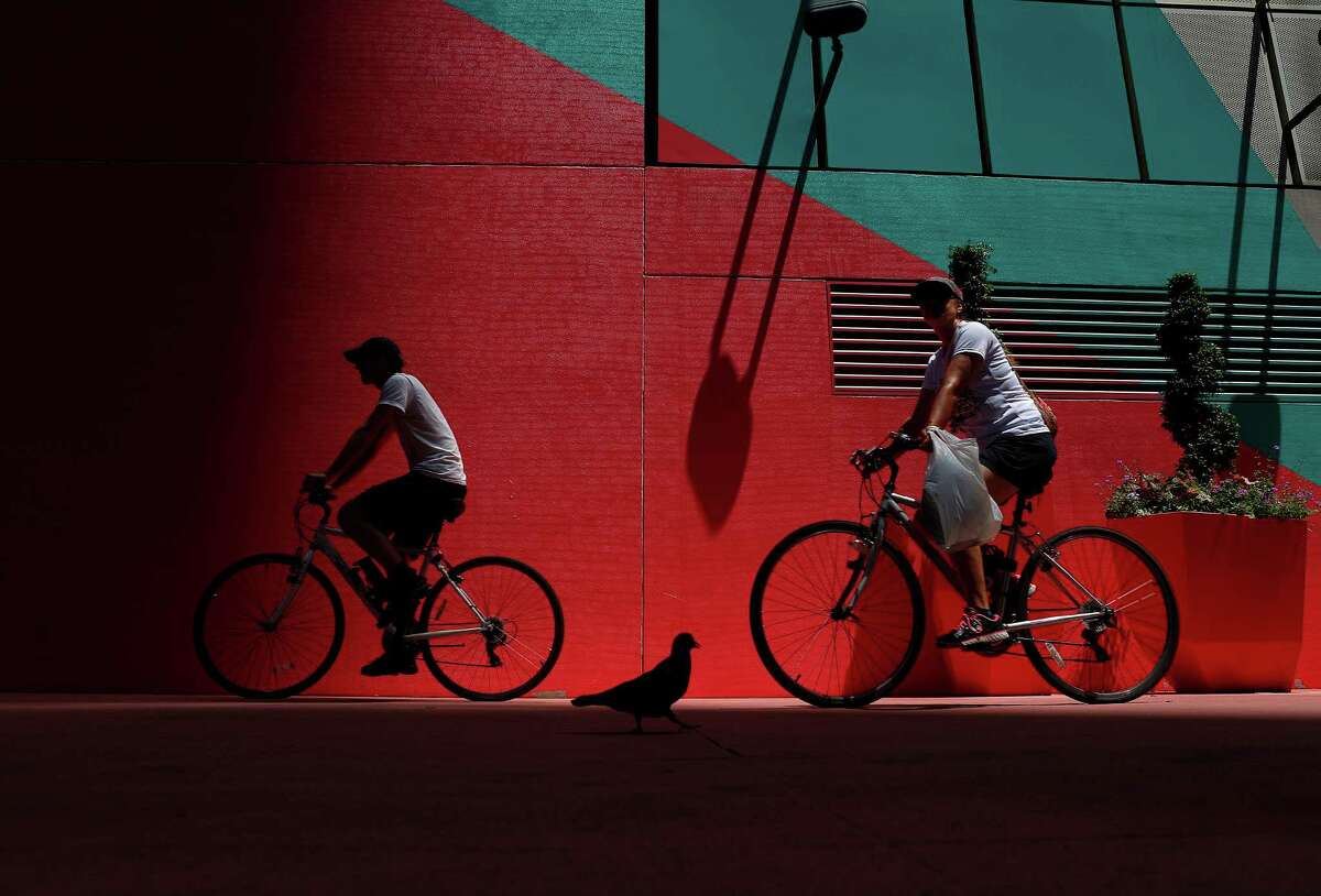 Bicyclists cycle along Main Street past a giant painting on a parking garage at the intersection with McKinney Street in downtown Houston. ( Mark Mulligan / Houston Chronicle )