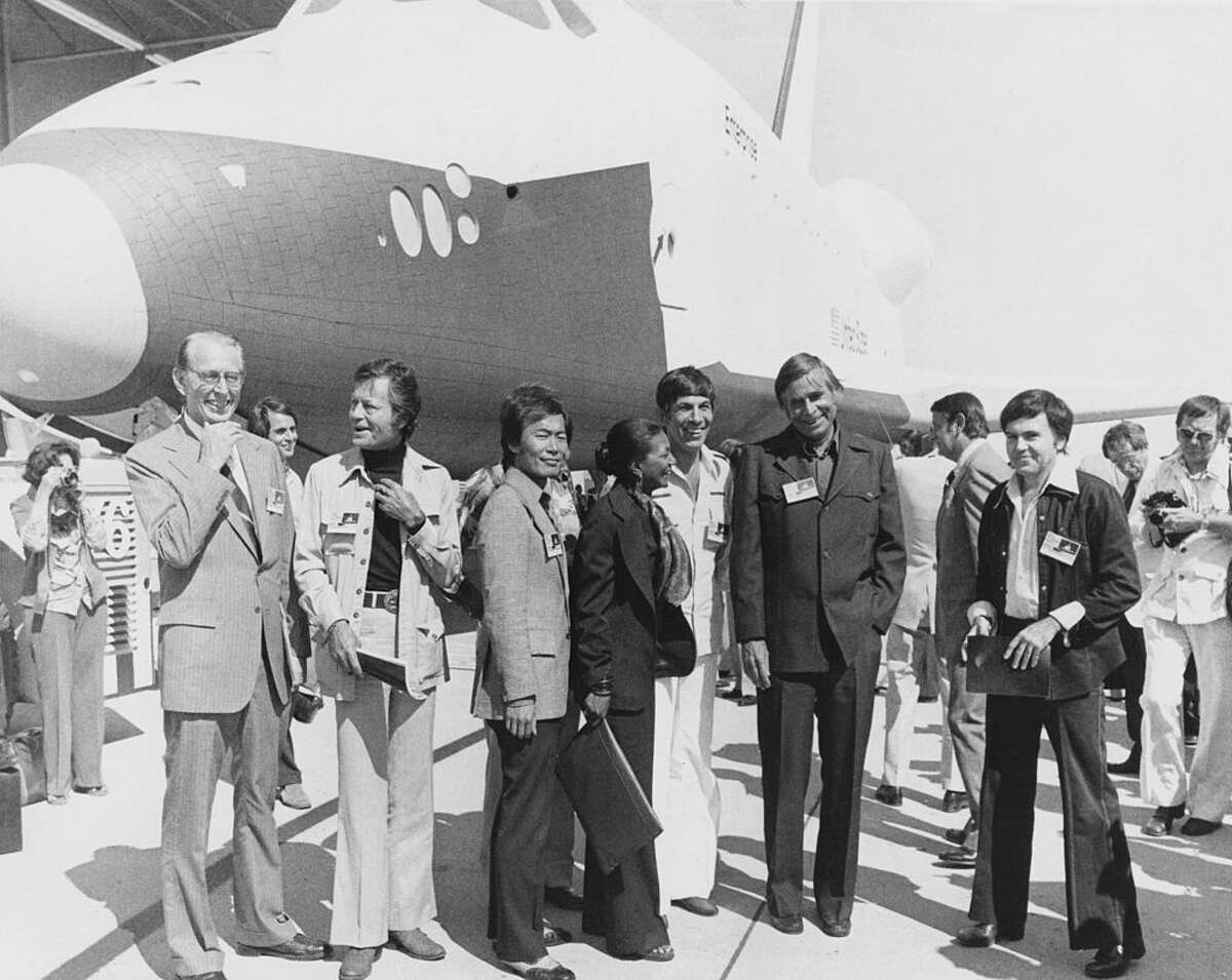 The space shuttle orbiter OV-101, aka 'Enterprise', is unveiled at the NASA/Rockwell International Space Division assembly plant at Palmdale, California, in the presence of the cast of hit tv show 'Star Trek', 17th September 1976. From left to right, NASA administrator Dr. James C. Fletcher, actors DeForest Kelley, George Takei, Nichelle Nichols, Leonard Nimoy, series creator Gene Roddenberry and actor Walter Koenig. (Photo by Space Frontiers/Getty Images)