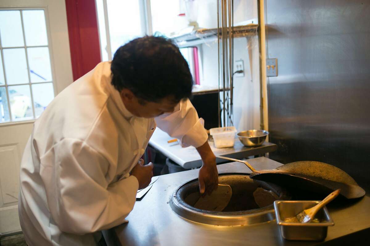 Perm Tamang quickly sticks naan to the inside of the oven at Cuisine of Nepal in S.F.
