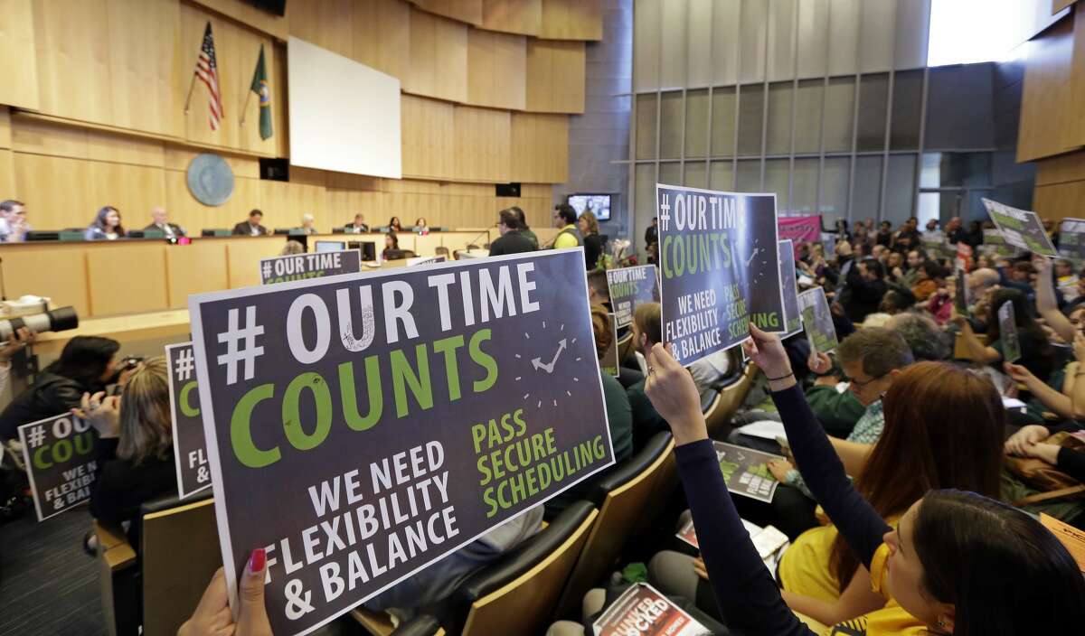 Supporters of new work scheduling rules hold up signs during a public comment period at a Seattle City Council meeting, Monday, Sept. 19, 2016, in Seattle. The Council was to vote Monday on new scheduling rules for hourly retail and food-service employees, including requiring employers to schedule shifts 14 days in advance and pay workers extra for certain last-minute scheduling changes. (AP Photo/Elaine Thompson)