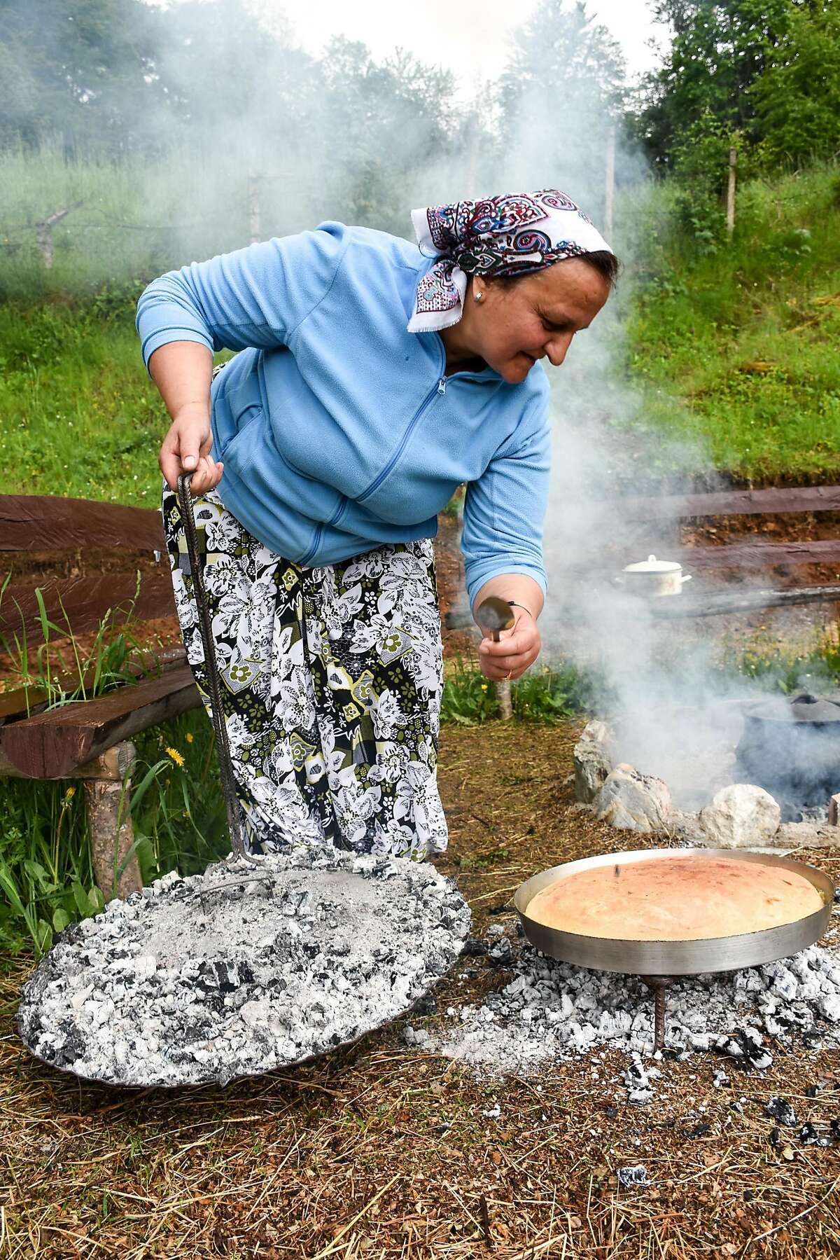 Halida Kurtishi bakes traditional Bosnian bread over coals in an outdoor pit for lunch.