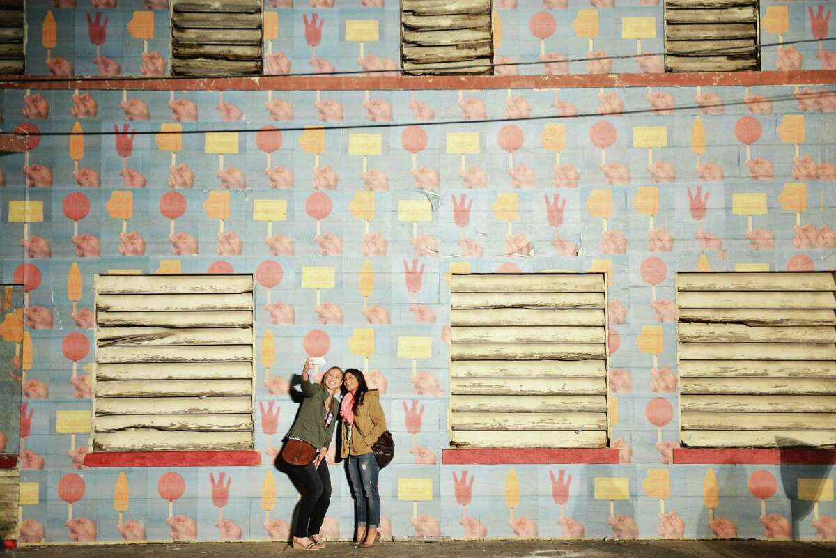 Kendra Erskine, left, and Cassie Rubio take a selfie next to a wall with Luminaria's design pasted on it during Luminaria near the Tobin Center for Performing Arts in San Antonio Nov. 7, 2014.