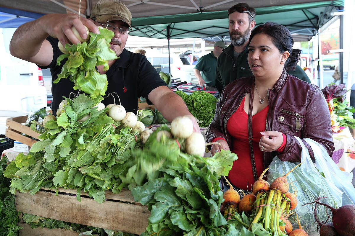 Fernando Vasquez (left) sells produce to Vianey Garcia as another customer, Mike Lee (center) waits his turn at the Yard Farmers and Ranchers Market on March 22, 2015.