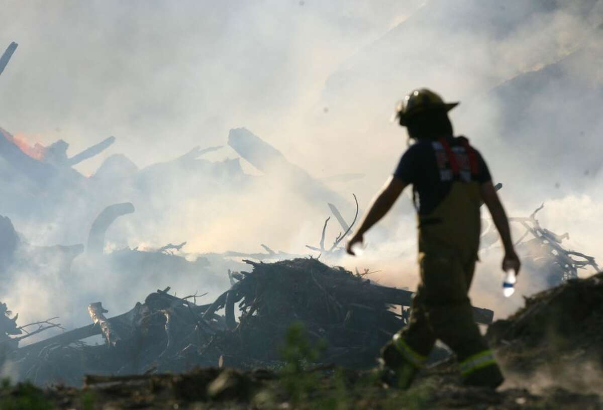 A firefighter walks across the scene of a large mulch yard fire Saturday on Highway 242 East in Conroe.