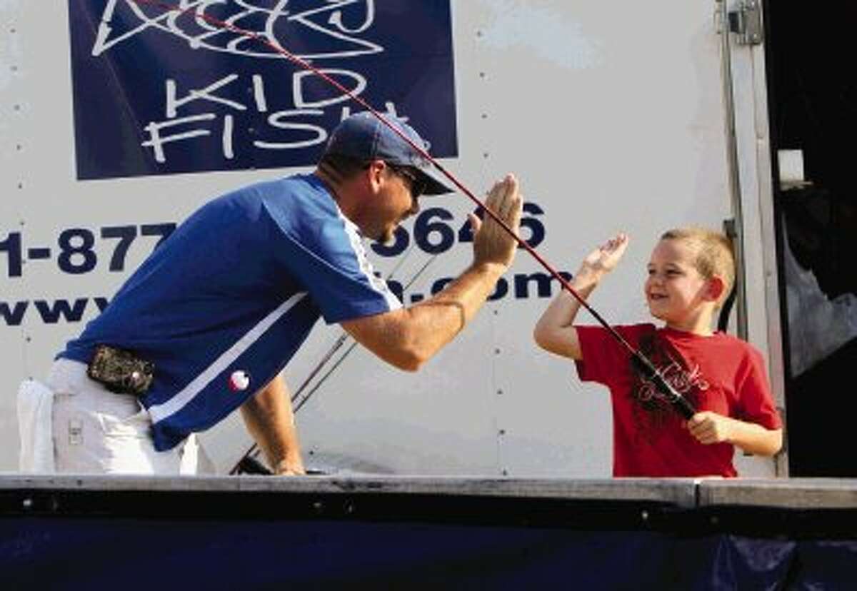 Brayden Weisinger gets a high-five from JP Brazeal after catching a catfish at the “Hooked on Chevy” event at Buckalew Chevrolet in Conroe Saturday. Children fished for catfish and earned T-shirts and tackle boxes for the number of fish they caught. Go to HCNPics.com to view and purchase this photo and others like it.
