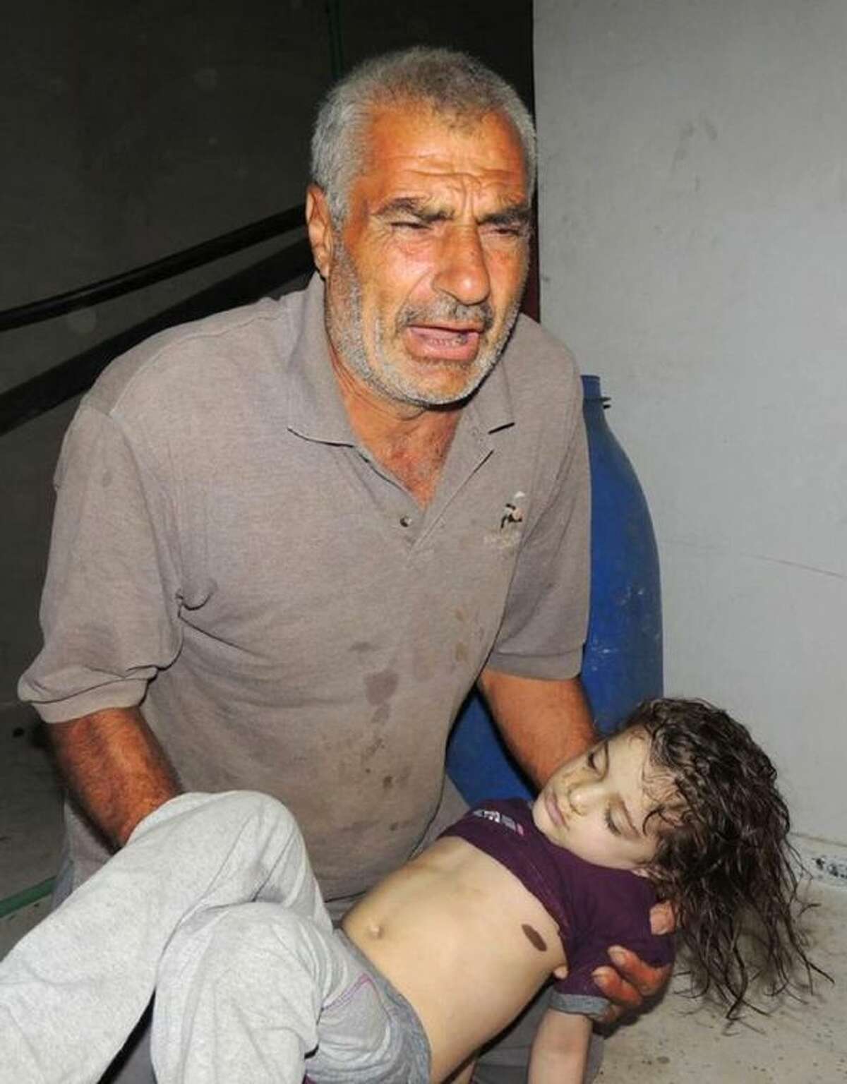 In this Aug. 21, 2013, file citizen journalism image provided by the Local Committee of Arbeen which has been authenticated based on its contents and other AP reporting, a Syrian man reacts as he carries a dead body of a Syrian girl, after an alleged poisonous gas attack fired by regime forces, according to activists in Arbeen town, Damascus, Syria. The early-morning barrage against rebel-held areas around the the Syrian capital Damascus immediately seemed different: The rockets made a strange, whistling noise. Seconds after one hit near his home, Qusai Zakarya says he couldn’t breathe, and he desperately punched himself in the chest to get air. Hundreds of suffocating, twitching victims flooded into hospitals. Others were later found dead in their homes, towels still on their faces from their last moments trying to protect themselves from gas. Doctors and survivors recount scenes of horror from the alleged chemical attack a week ago.