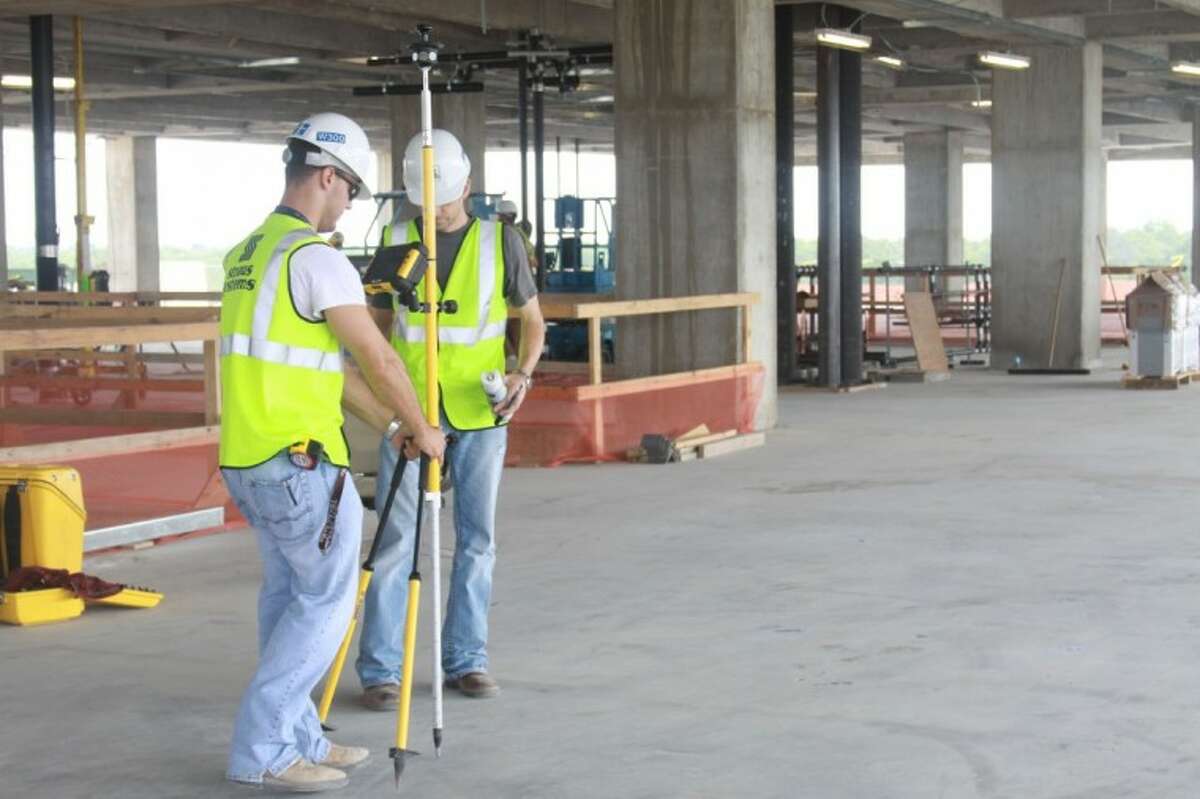 Using GPS, two workers mark areas on the concrete floor of Building 4 to indicate where ductwork will be installed for the building’s air-conditioning system.