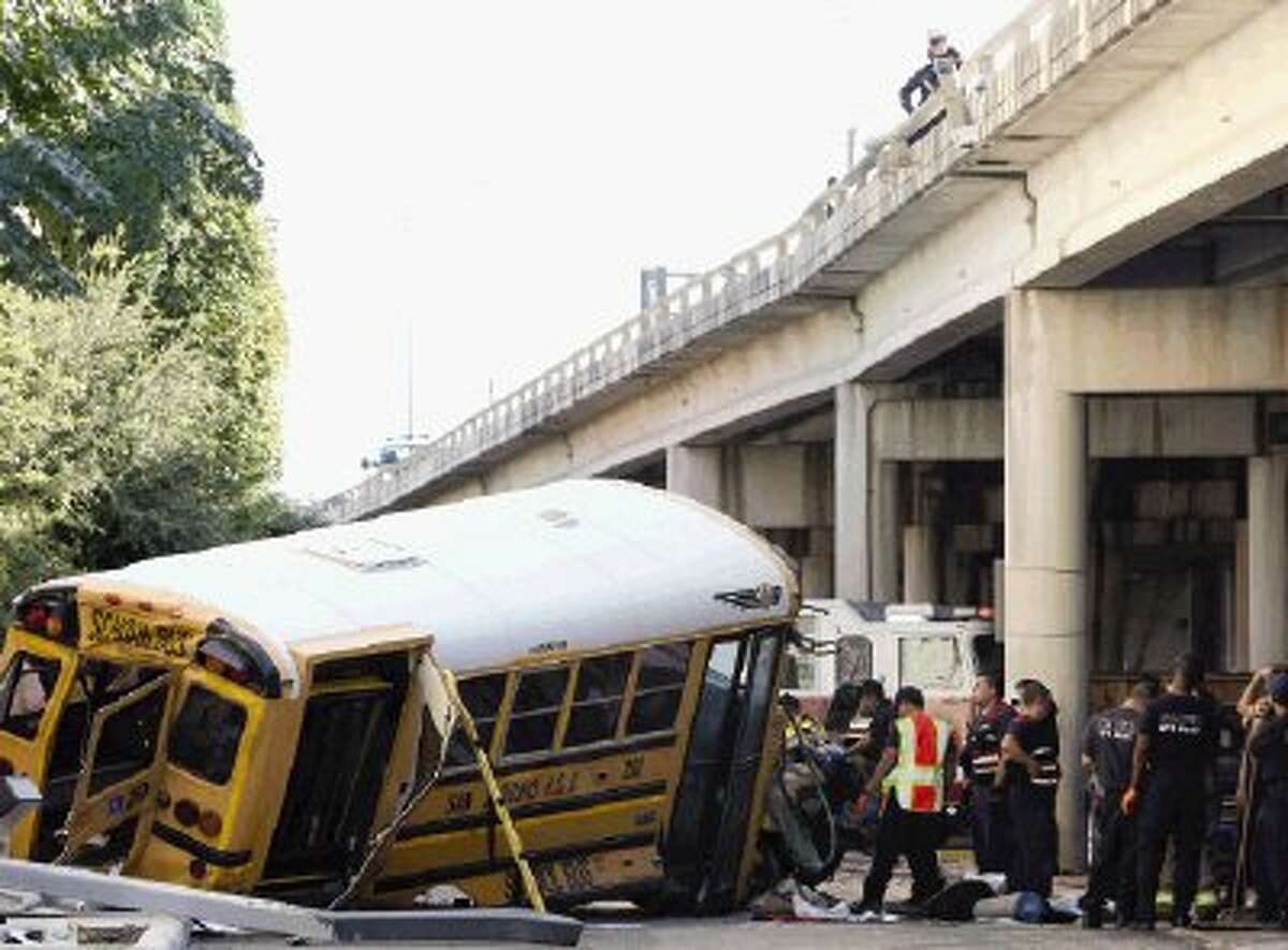 Emergency responders clean up after a collision caused a San Antonio ISD school bus to crash through a guardrail and fall off an elevated portion of Interstate 37 near Houston Street in downtown San Antonio, Texas. The school bus plunged about 15 feet from a Texas expressway overpass to the doorstep of a hotel below, miraculously causing only non-life-threatening injuries to the child and two adults aboard. (AP Photo/San Antonio Express-News, Helen L. Montoya)
