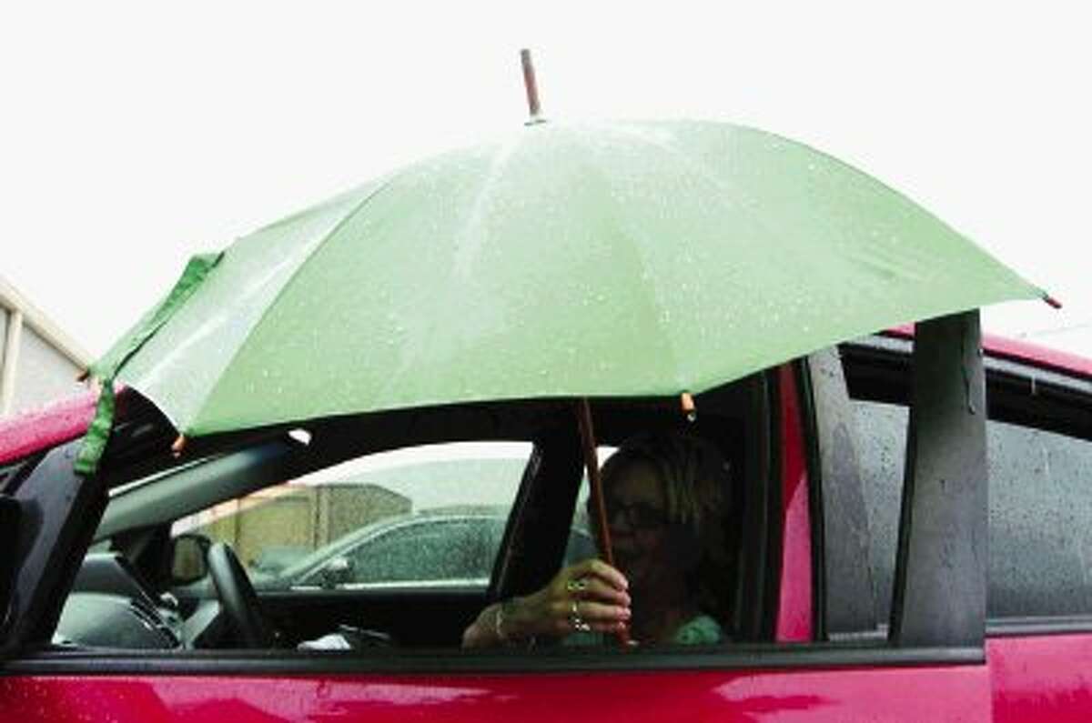 Debbie Wells adjusts an umbrella as she reads in her car during a break from work in Conroe Friday. The area has a 70 percent chance of thunderstorms today with a chance of storms continuing through Monday.