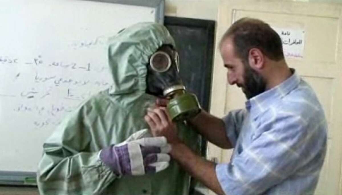 This image made from an AP video posted on Wednesday shows a volunteer adjusting a gas mask and protective suit on a student during a classroom session a on how to respond to a chemical weapons attack in Aleppo, Syria.
