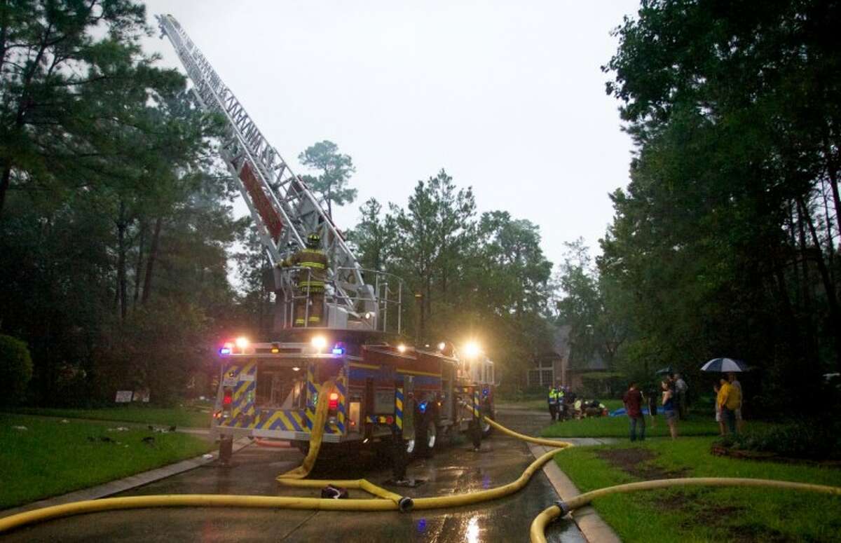 A ladder truck aids firefighters in fighting a 2-alarm residential fire thought to have been started by a lighting strike as neighbors look on Tuesday afternoon on Acadia Branch Place in The Woodlands.