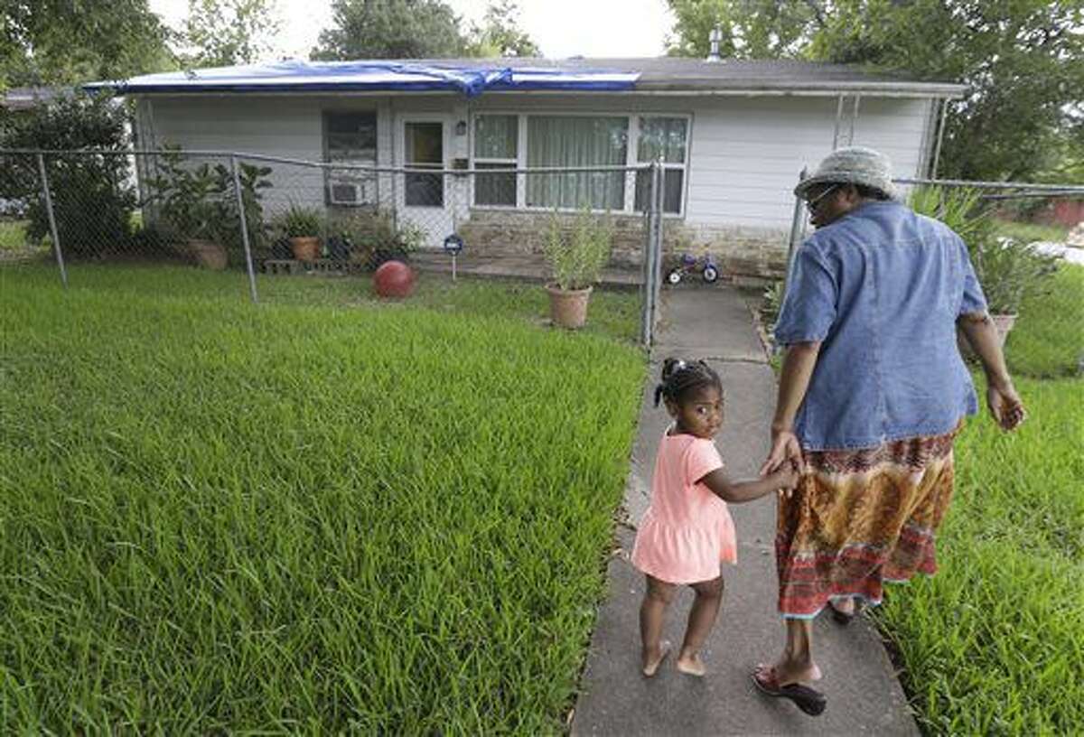 In this Wednesday, Sept. 7, 2016 photo, Wendlyn Hill walks with her great granddaughter, Harmony Wolfe, 2, outside her home where a blue tarp partially covers the roof in Houston. She has applied for help from the City of Houston for roof repairs. (Melissa Phillip/Houston Chronicle via AP)