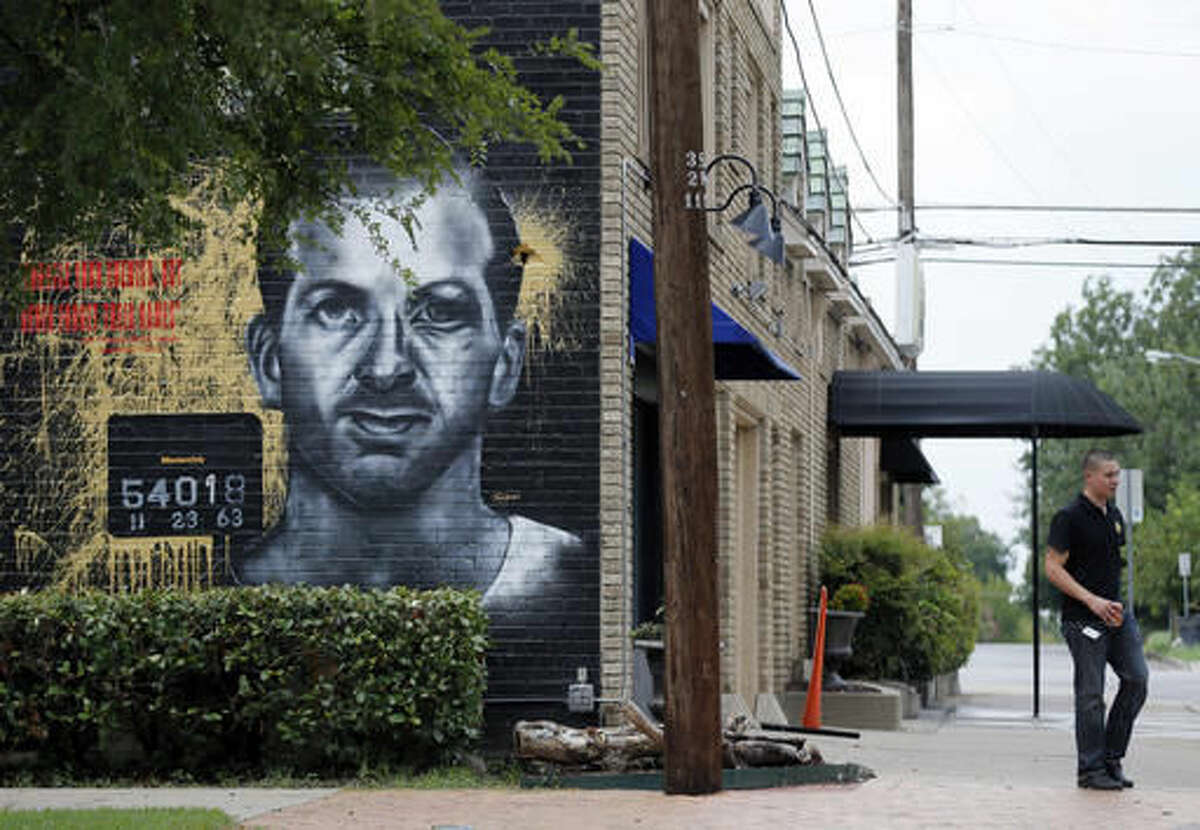 A person walks along the sidewalk by a mural of Lee Harvey Oswald painted on an exterior wall outside the Members Only barbershop, Friday, Aug. 26, 2016, in Dallas. Barbershop owner Christian Avanti hired an artist to paint the black and white mural with a John F. Kennedy quote over it, "Forgive your enemies, but never forget their names". (AP Photo/Tony Gutierrez)