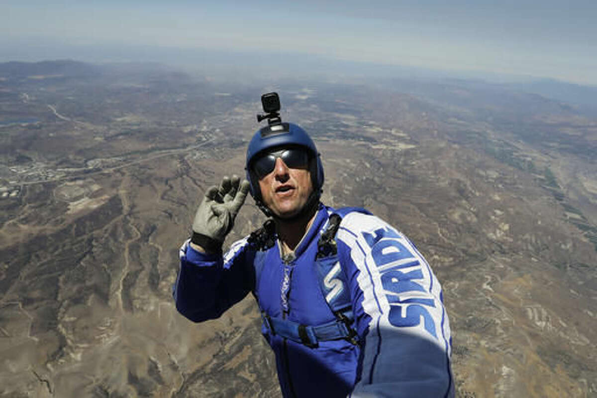 In this Monday, July 25, 2016 photo, skydiver Luke Aikins signals to pilot Aaron Fitzgerald as he prepares to jump from a helicopter in Simi Valley, Calif. After months of training, this elite skydiver says he's ready to leave his chute in the plane when he bails out 25,000 feet over Simi Valley on Saturday. That's right, no parachute, no wingsuit and no fellow skydiver with an extra one to hand him in mid-air. (AP Photo/Jae C. Hong)