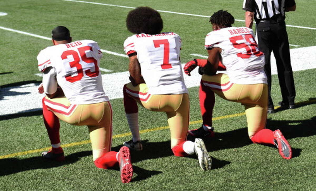 Free safety Eric Reid, quarterback Colin Kaepernick, and outside linebacker Eli Harold of the San Francisco 49ers kneel on the sidelines during the national anthem before the game against the Seattle Seahawks at CenturyLink Field on September 25, 2016 in Seattle.