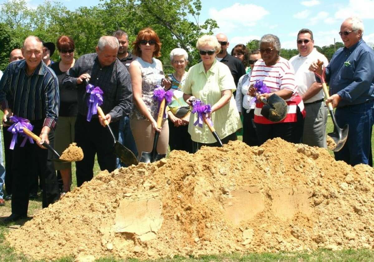 With supportive Dayton Rotary Club members and other members of the community gathered behind them, shovelers break ground -- one might say break mound -- on the southeast side of the Dayton Community Center where a helipad will be installed. Digging in, from left, are Rotary Heliport Committee Chairman Ken DeFoor, Rotary President Brooks Hiller, Dayton City Council members Anita Brown, Barbara Zaruba and Eliza Mae Guidry, who is mayor pro tem, and Dayton Mayor Felix Skarpa.