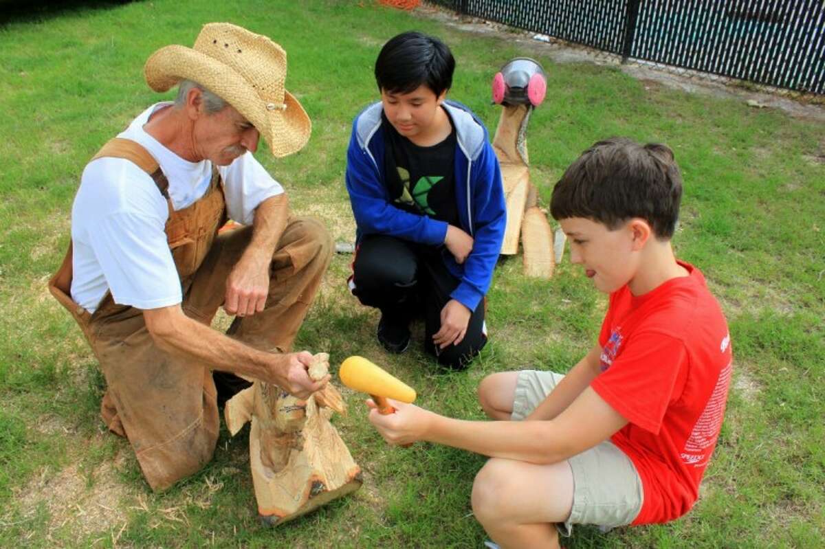 Artist James D. Phillips shows Bleyl Middle School 6th-graders Dereck Lam (center) and Sam Shouse how to do detail work on a wood sculpture